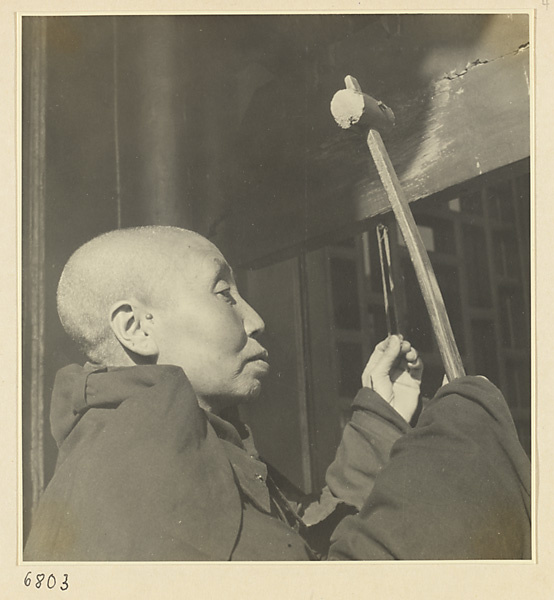 Buddhist nun striking a board with a wooden mallet
