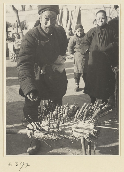Street vendor hawking candied fruit called tang hu lu from a pole stand