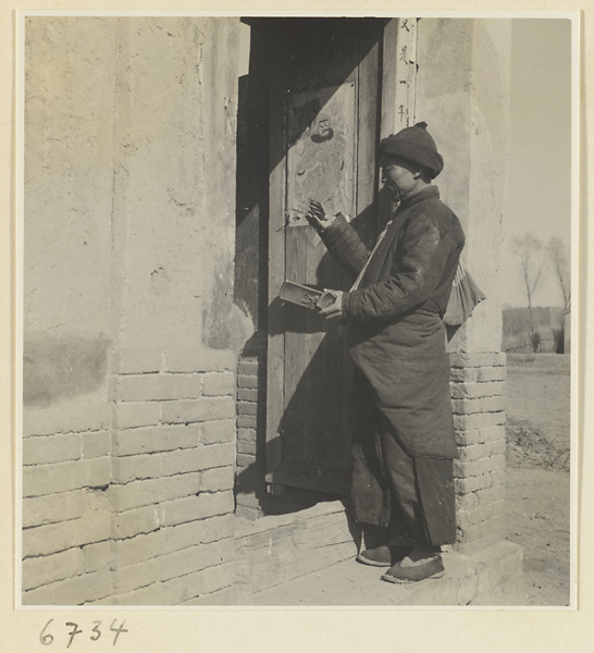 Itinerant story teller with wooden castanets at the door of a house with couplets and a picture of a door god