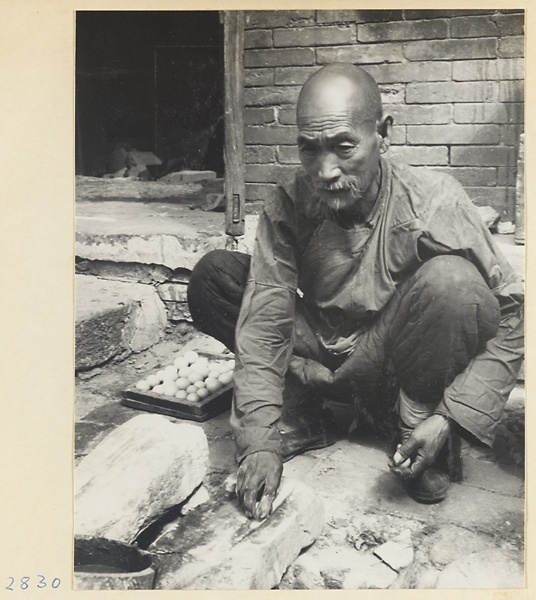 Man smoothing pieces of marble into balls using a stone drainpipe at Tan zhe si