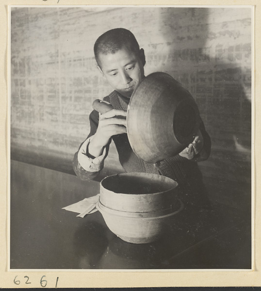 Interior of a scroll-mounting shop showing a man pouring thinned paste called hu or jiang hu into a horsehair strainer