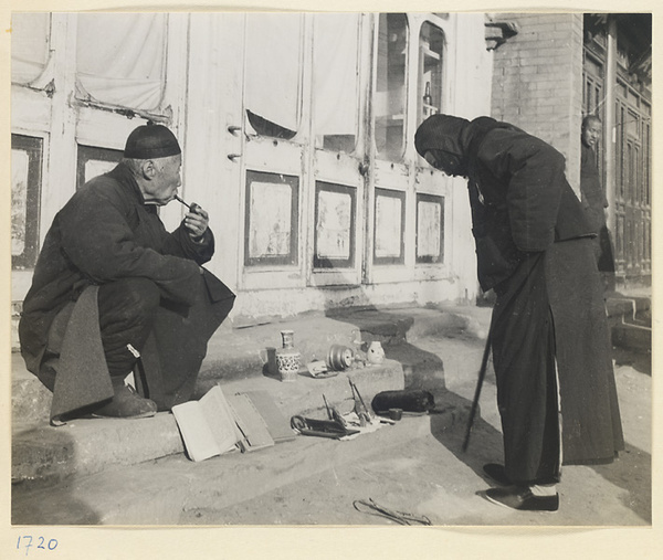 Man sitting on steps of a building smoking and hawking books and decorative objects