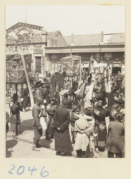 Spectators watching members of a wedding procession carrying umbrellas, fan-shaped screen and draped mirrors and playing musical instruments