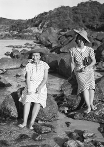 Maggie Henderson and Lucy Hutchinson, both bare-footed and sitting on the rocks of a bay, at a beach, Hong Kong