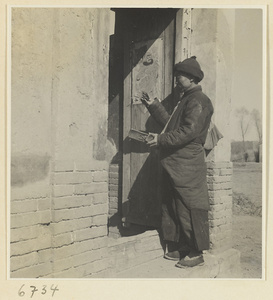 Itinerant story teller with wooden castanets at the door of a house with couplets and a picture of a door god