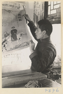 Man in a scroll-mounting shop removing a rebacked scroll painting from a drying board called a zhuang ban