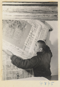 Man in a scroll-mounting shop moving a scroll painting attached to a drying board called a zhuang ban
