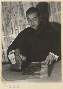 Man in a scroll-mounting shop using a brush to adhere a painting on silk onto a backing