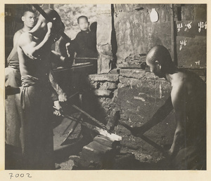 Men hammering heated metal at a forge in a wheel-making shop