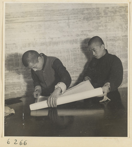 Interior of a scroll-mounting shop showing two men working on a scroll painting