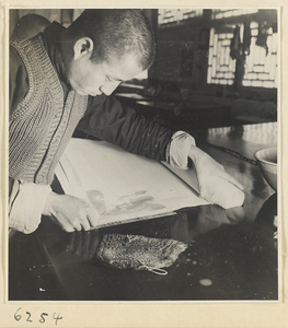 Interior of a scroll-mounting shop showing a man working on a scroll painting