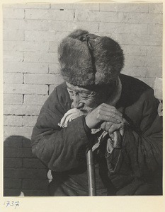 Seated man with fur hat leaning on his cane