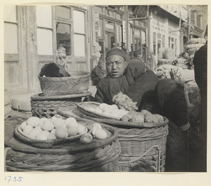 Street vendor reclining next to baskets displaying food for sale