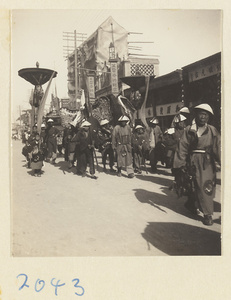 Members of a wedding procession carrying furled umbrellas and fan-shaped screen