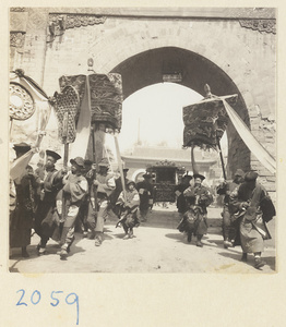 Members of a wedding procession carrying draped mirror, fan-shaped screen, umbrellas, and sedan chair through city gate