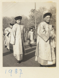 Members of a funeral procession wearing silk robes and fur hats