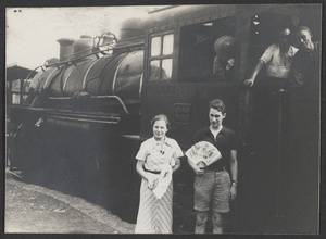 Western woman and man with fans standing next to locomotive and engineers