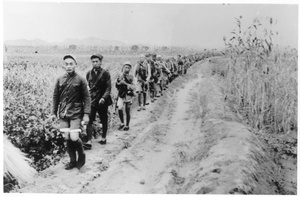 Soldiers marching in single file on a path between fields