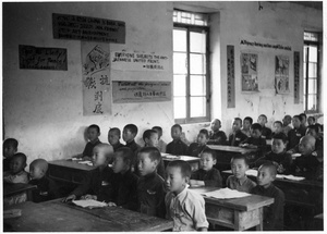 Children in a school room, with slogans on posters in Chinese and English on the wall