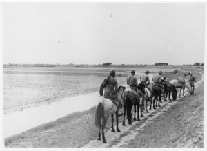 Six soldiers on horseback in single file on a track