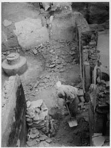 An old man burying his possessions in a ruined building, after hearing of the approach of Japanese forces, 1942